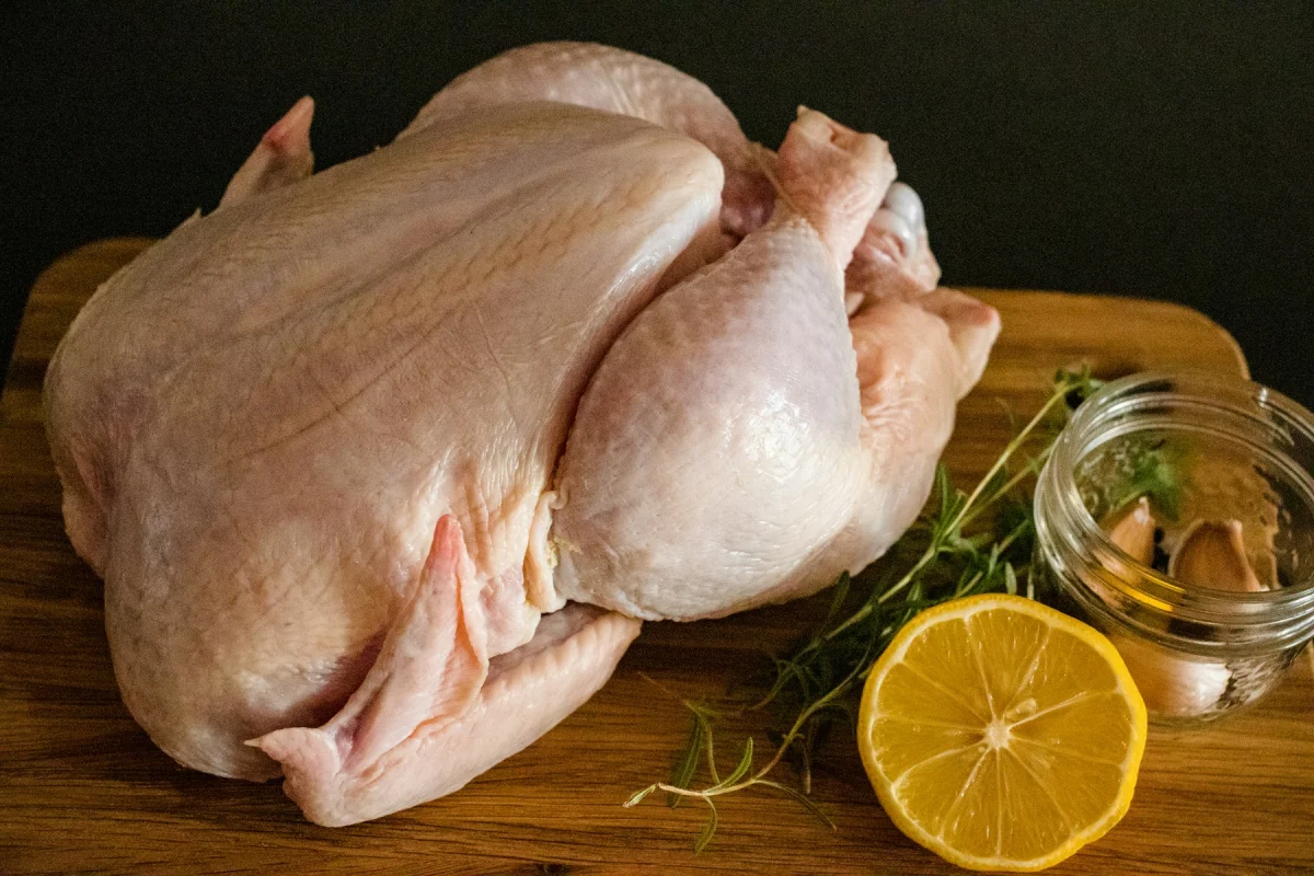 Whole raw chicken on a wooden cutting board with lemon and fresh rosemary